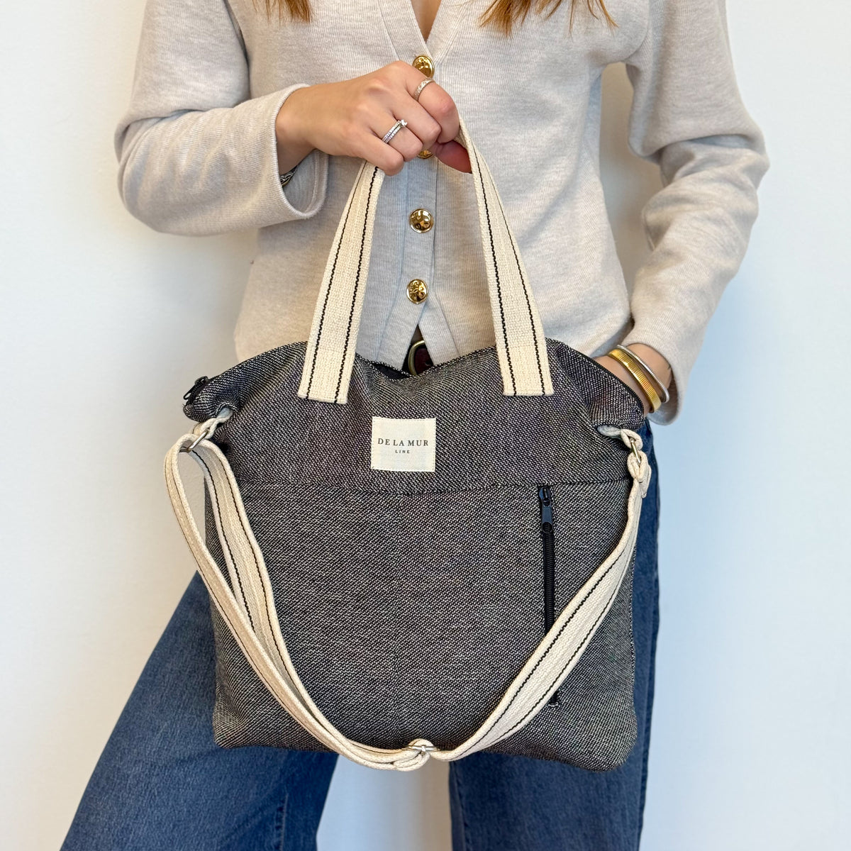 Model holding the DE LA MUR Sinay handbag by the handles, three-quarter view