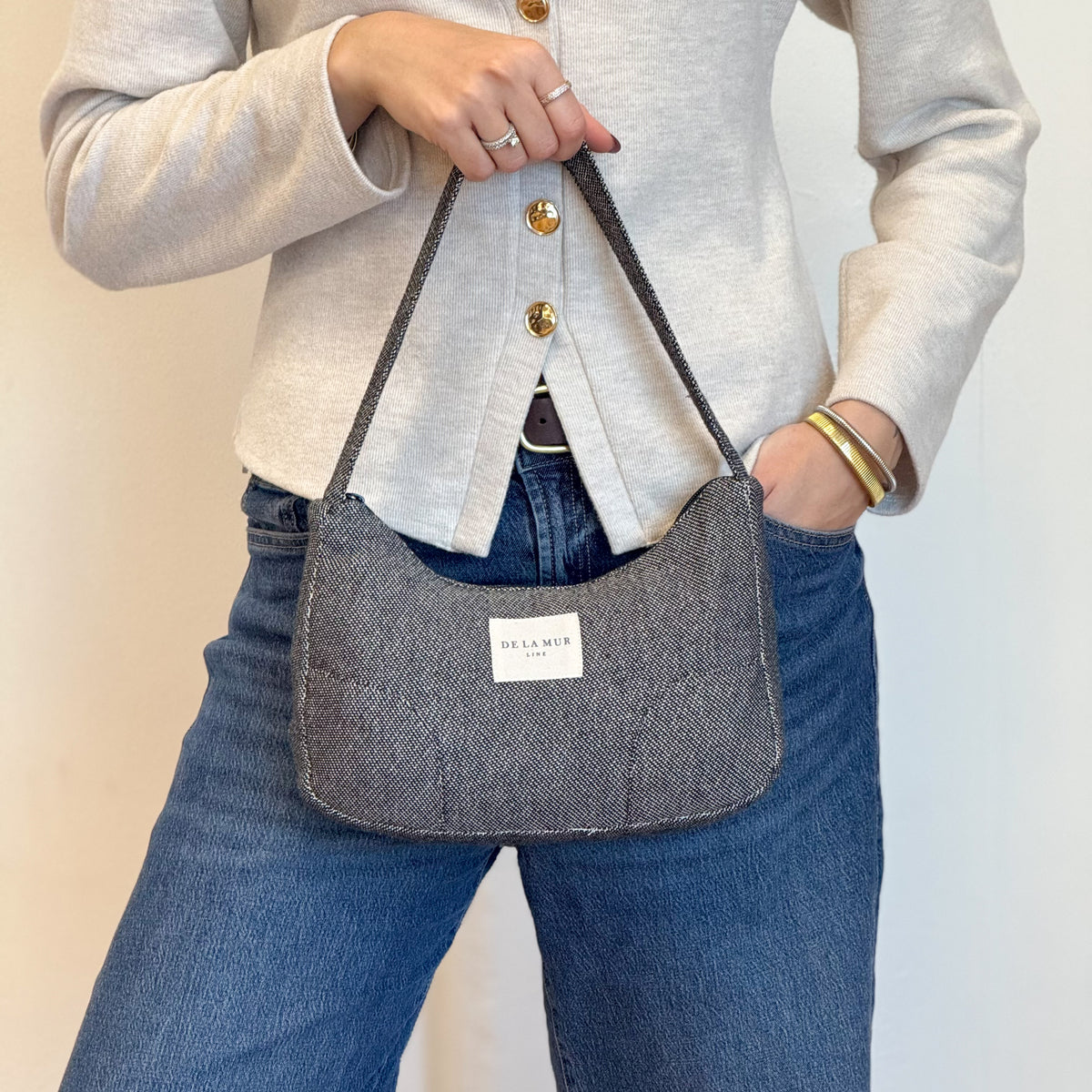 Model holding the DE LA MUR Sinay black shoulder bag over jeans, lifestyle shot
