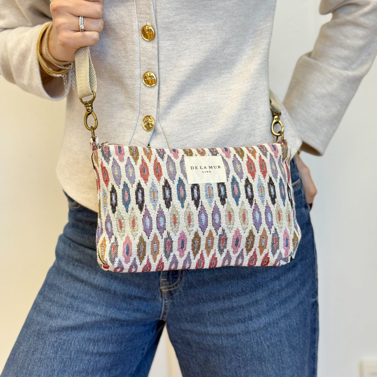 Model carrying the DE LA MUR Urban geometric jacquard clutch crossbody over jeans