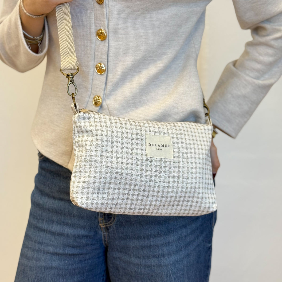 Model carrying the DE LA MUR Vison gingham jacquard clutch crossbody over jeans