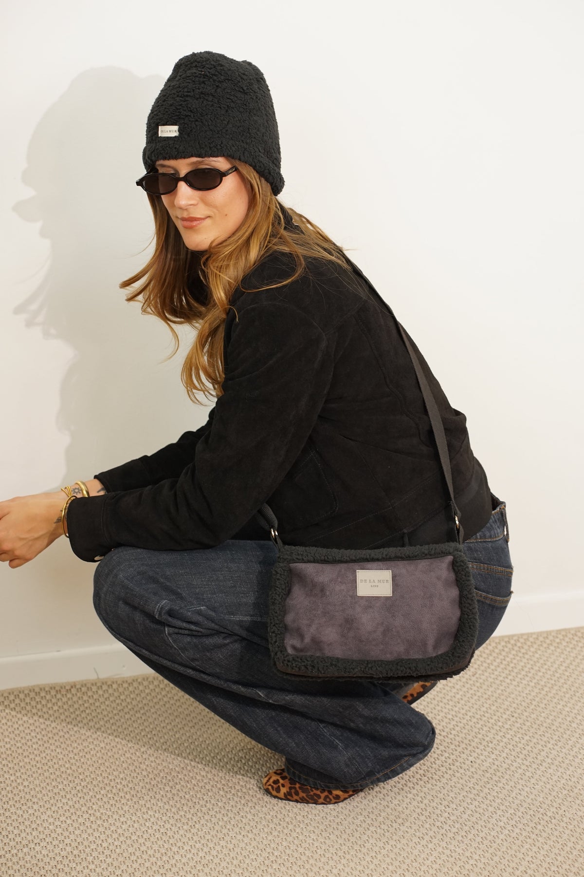 Model crouching, showing the back of the DE LA MUR Cene small shoulder bag