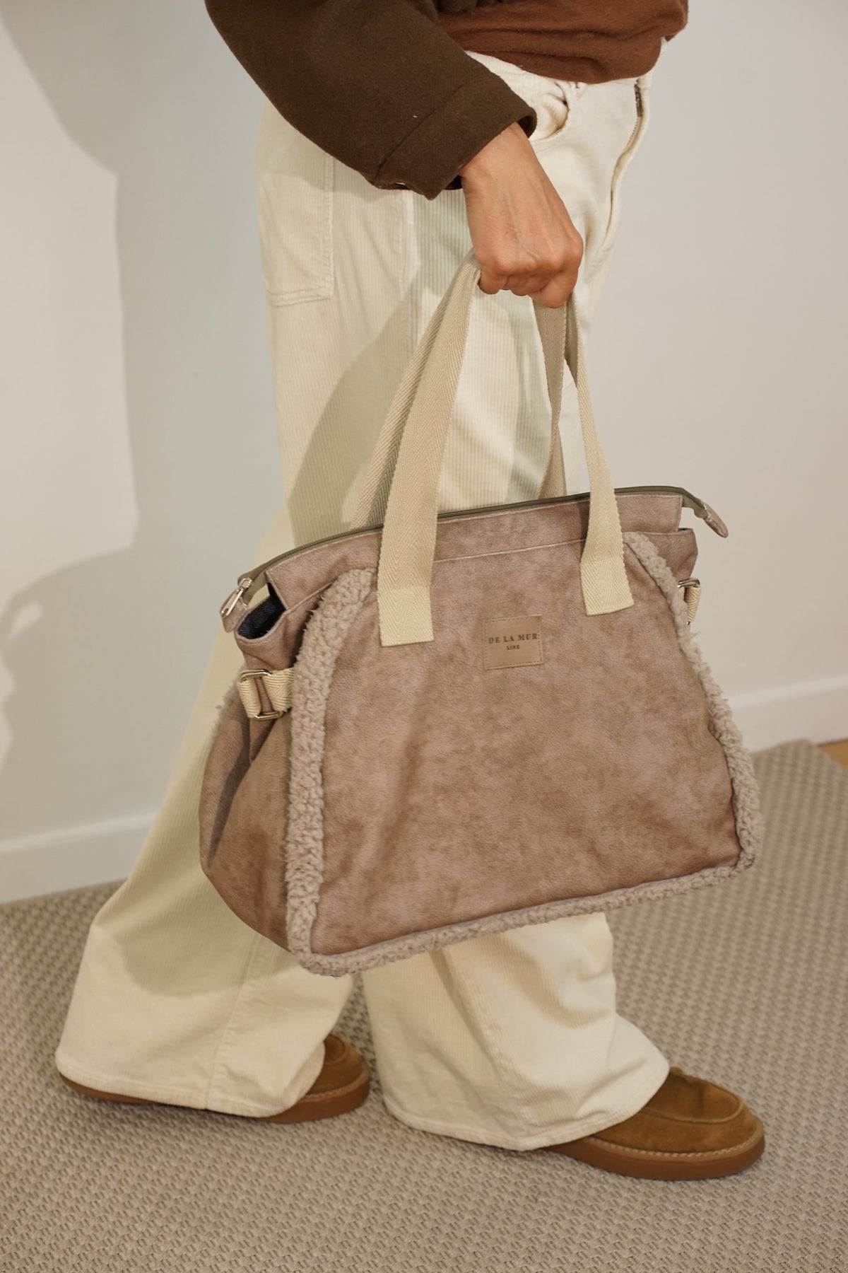 DE LA MUR Noce faux suede large shoulder bag held by hand, front view with brand patch