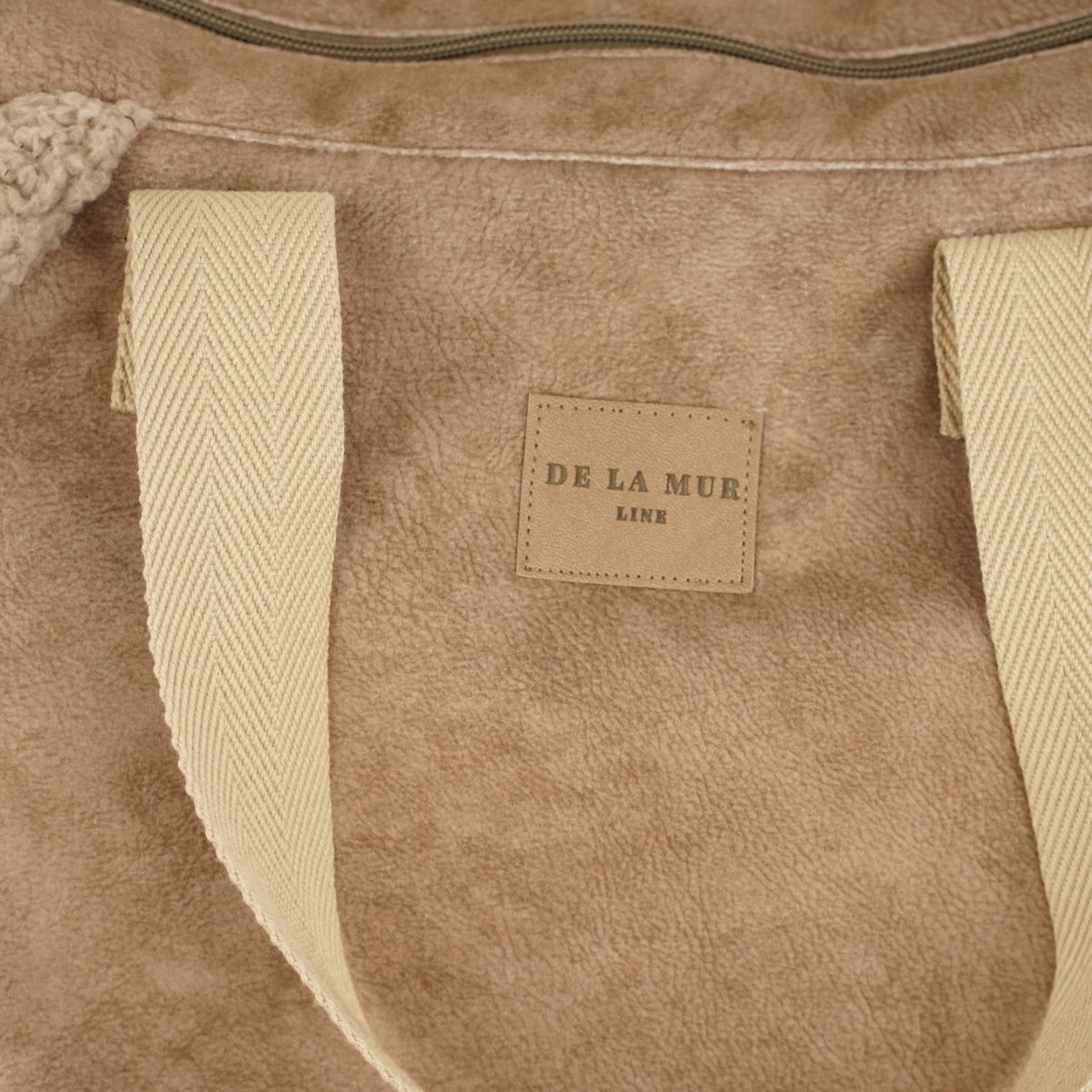 Close-up of the DE LA MUR Line leather label on the taupe Noce shoulder bag