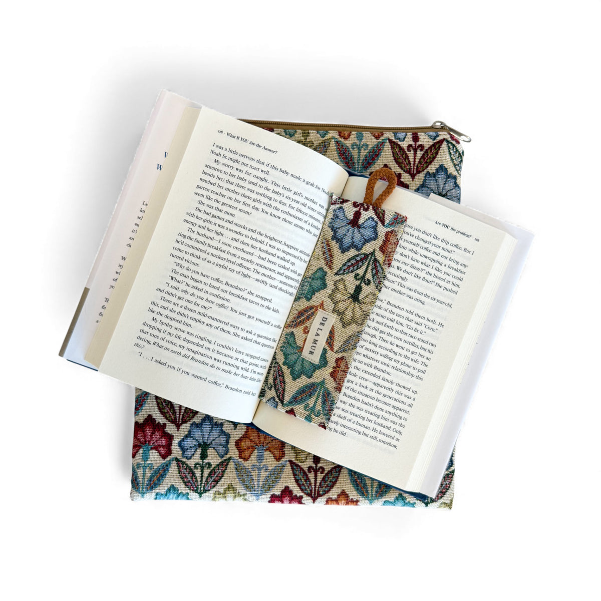 Open book with the DE LA MUR Flora floral bookmark resting on the book cover