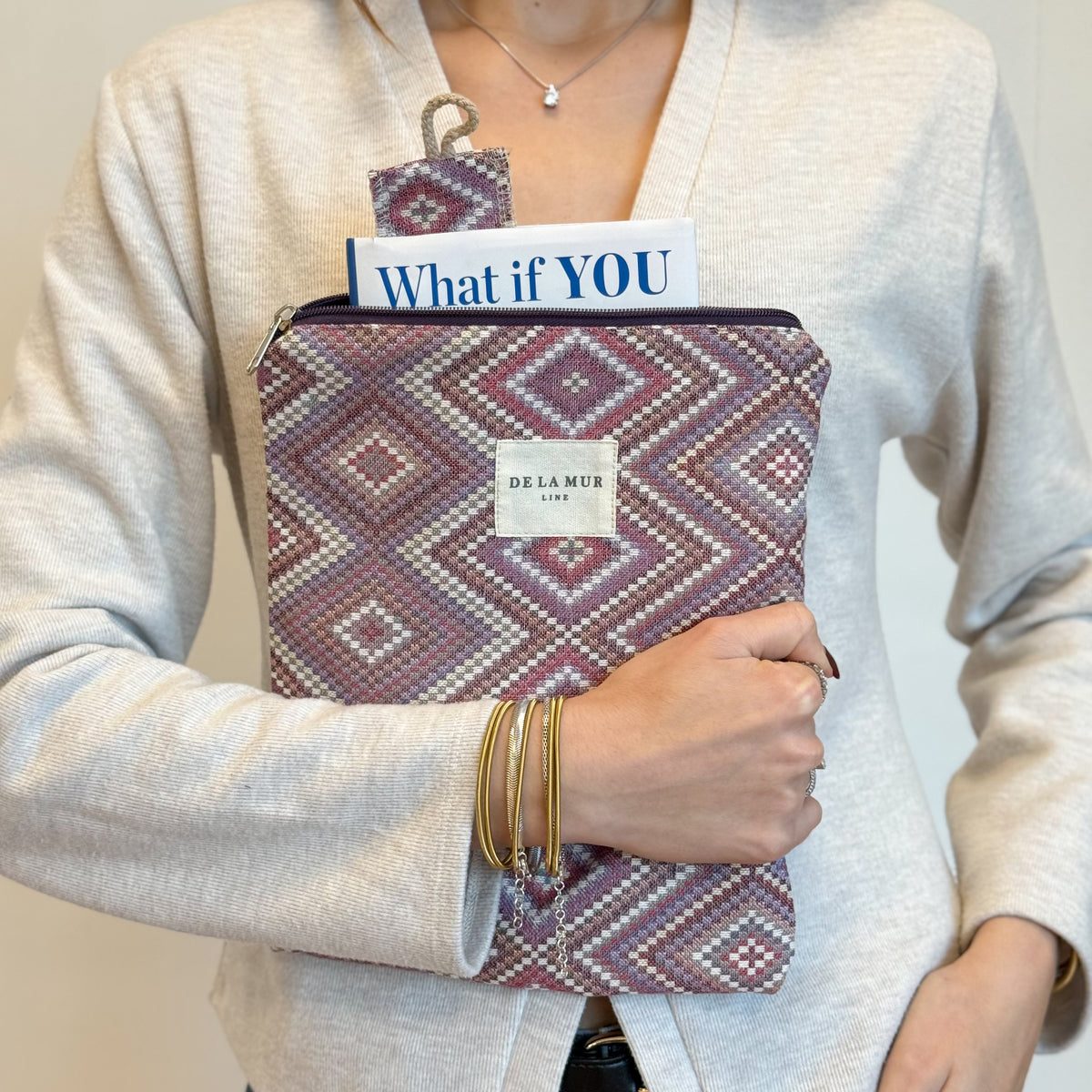 Model carrying the DE LA MUR Nana geometric book cover and bookmark against her cardigan