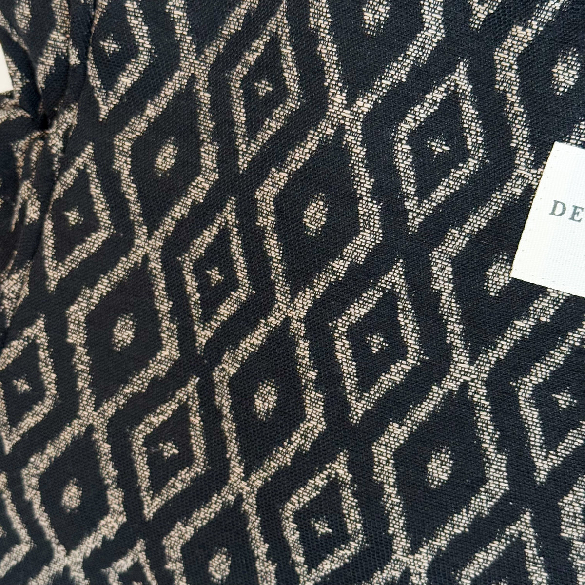 Close-up of the black and beige diamond geometric jacquard fabric and DE LA MUR label