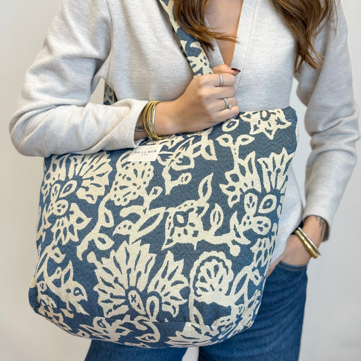 Model holding the DE LA MUR Akay floral tote with callouts for shoulder straps and zip closure