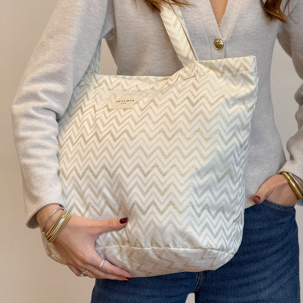 Model holding the gold zigzag DE LA MUR Astro tote, three-quarter view