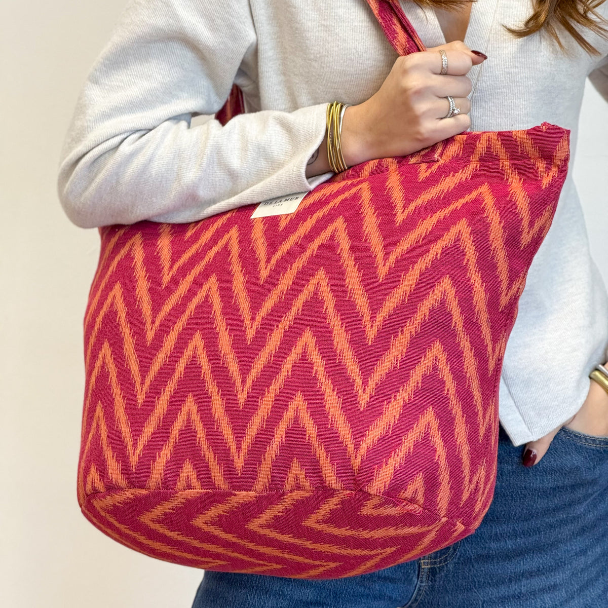 Model holding the pink and orange DE LA MUR Fuego tote, side view