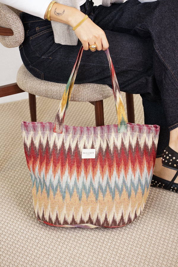 DE LA MUR Guana zigzag jacquard large zippered bag held by its handles, close lifestyle view