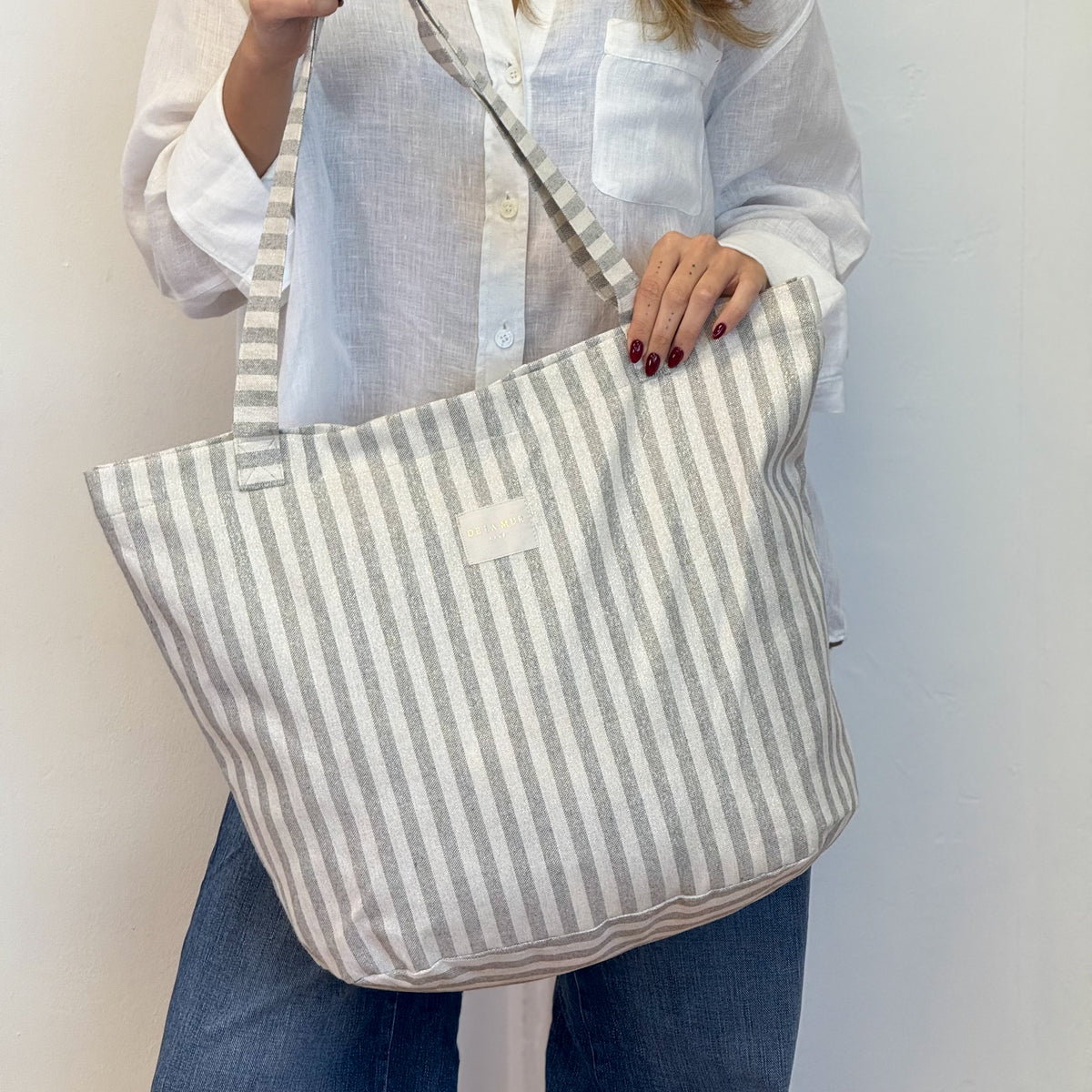 Model wearing the DE LA MUR gray striped tote bag over the shoulder
