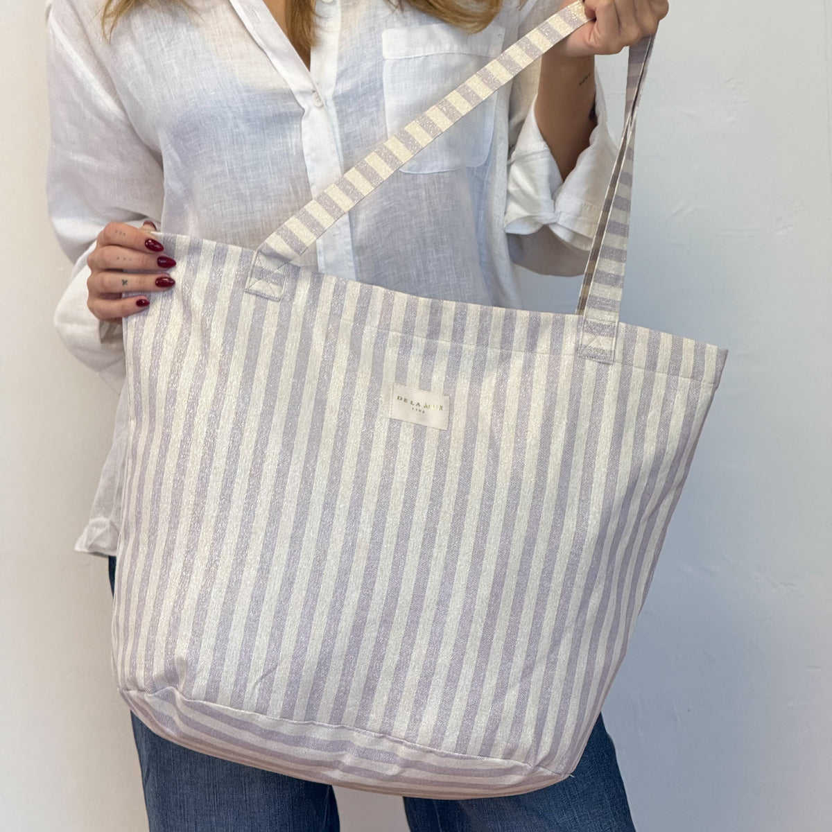 Model wearing the DE LA MUR lilac striped tote bag over the shoulder