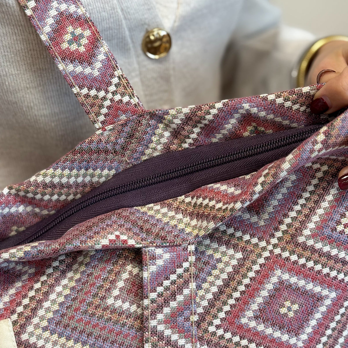 Detail of the DE LA MUR Nana tote zip closure and Line label held by a model