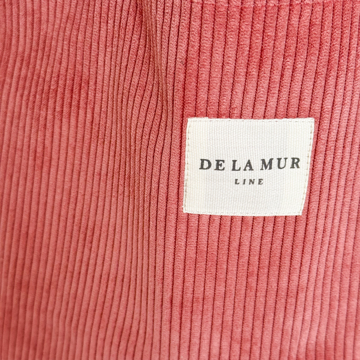 Close-up of coral corduroy fabric and DE LA MUR Line label