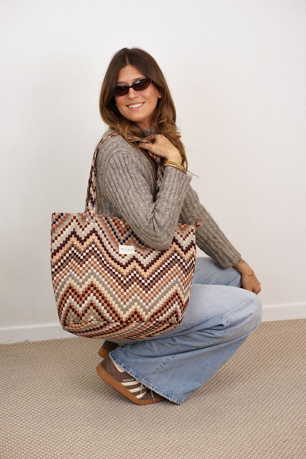 Model with DE LA MUR Pier zigzag jacquard tote bag in brown and beige on shoulder, lifestyle shot