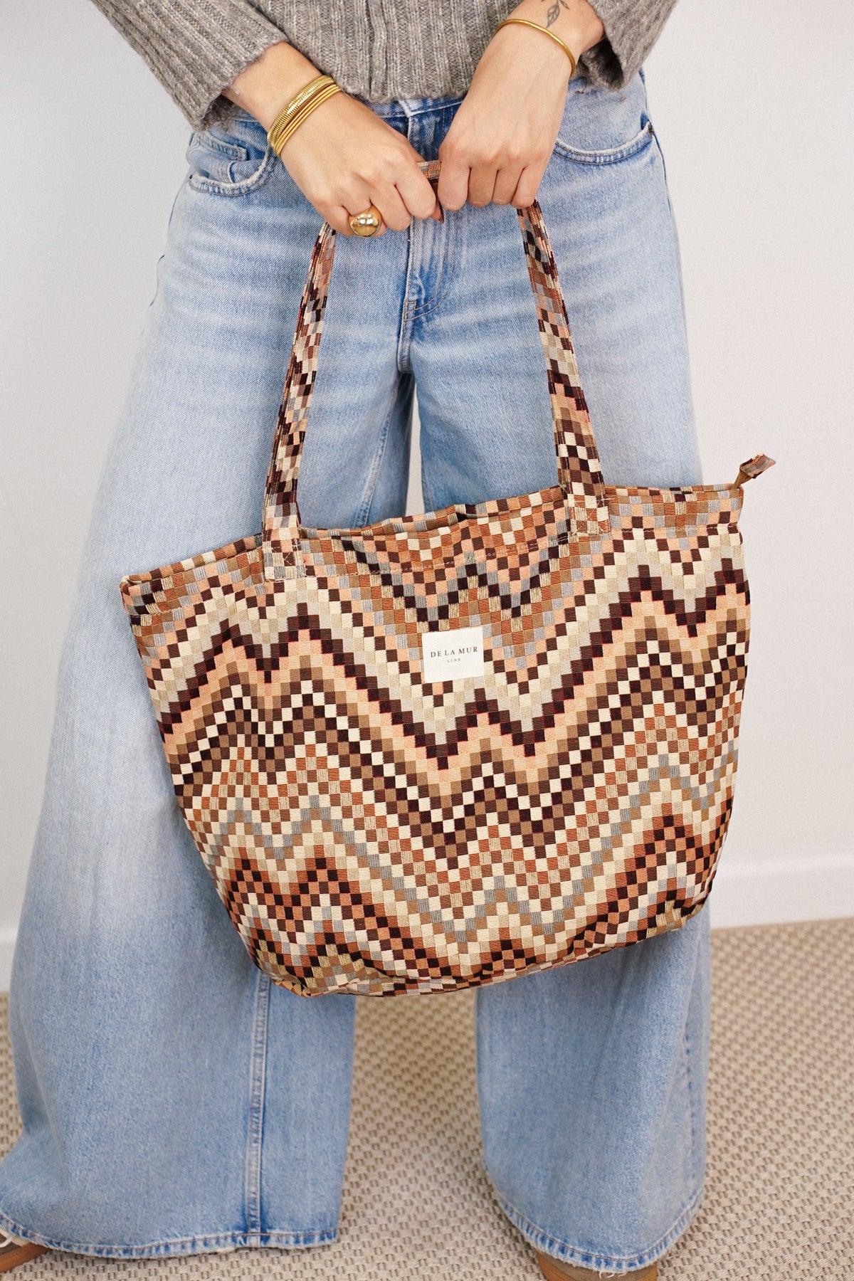 Model holding DE LA MUR Pier zigzag jacquard tote bag by the handles, lifestyle view