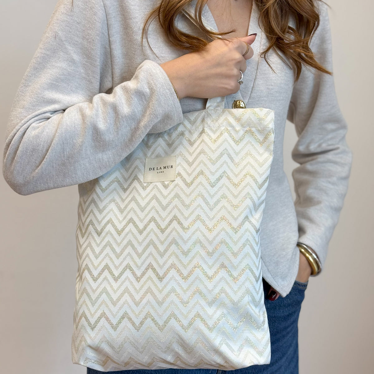 Model holding the DE LA MUR gold zigzag zippered bag by the strap