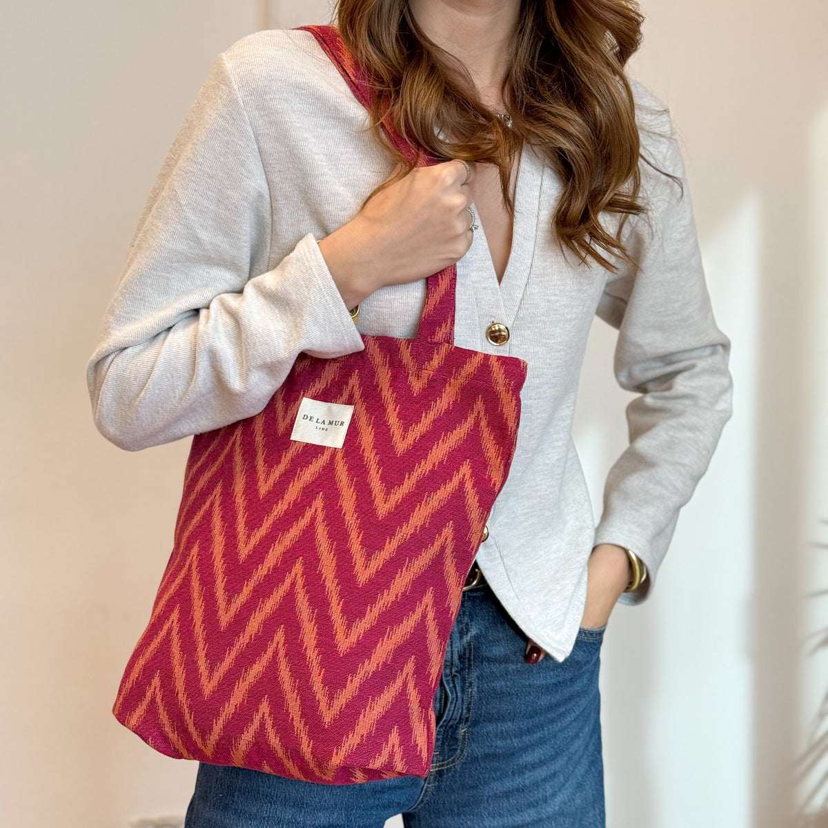 Model holding the DE LA MUR Fuego pink and orange zigzag tote, close shot