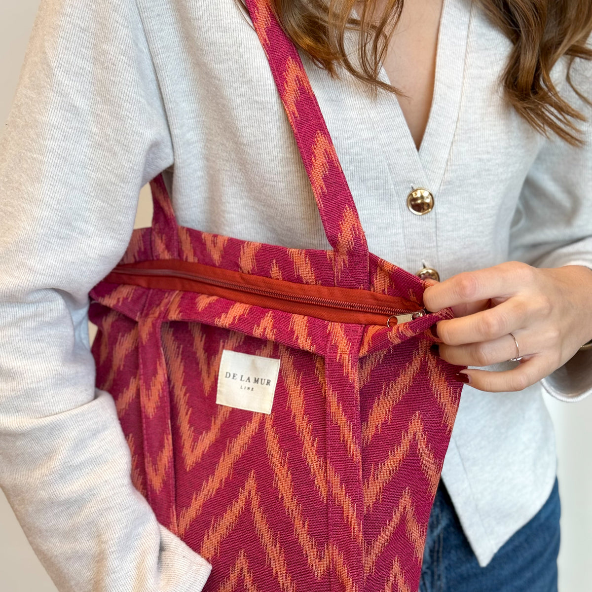 Hands opening the zip of the DE LA MUR Fuego bag worn on the shoulder