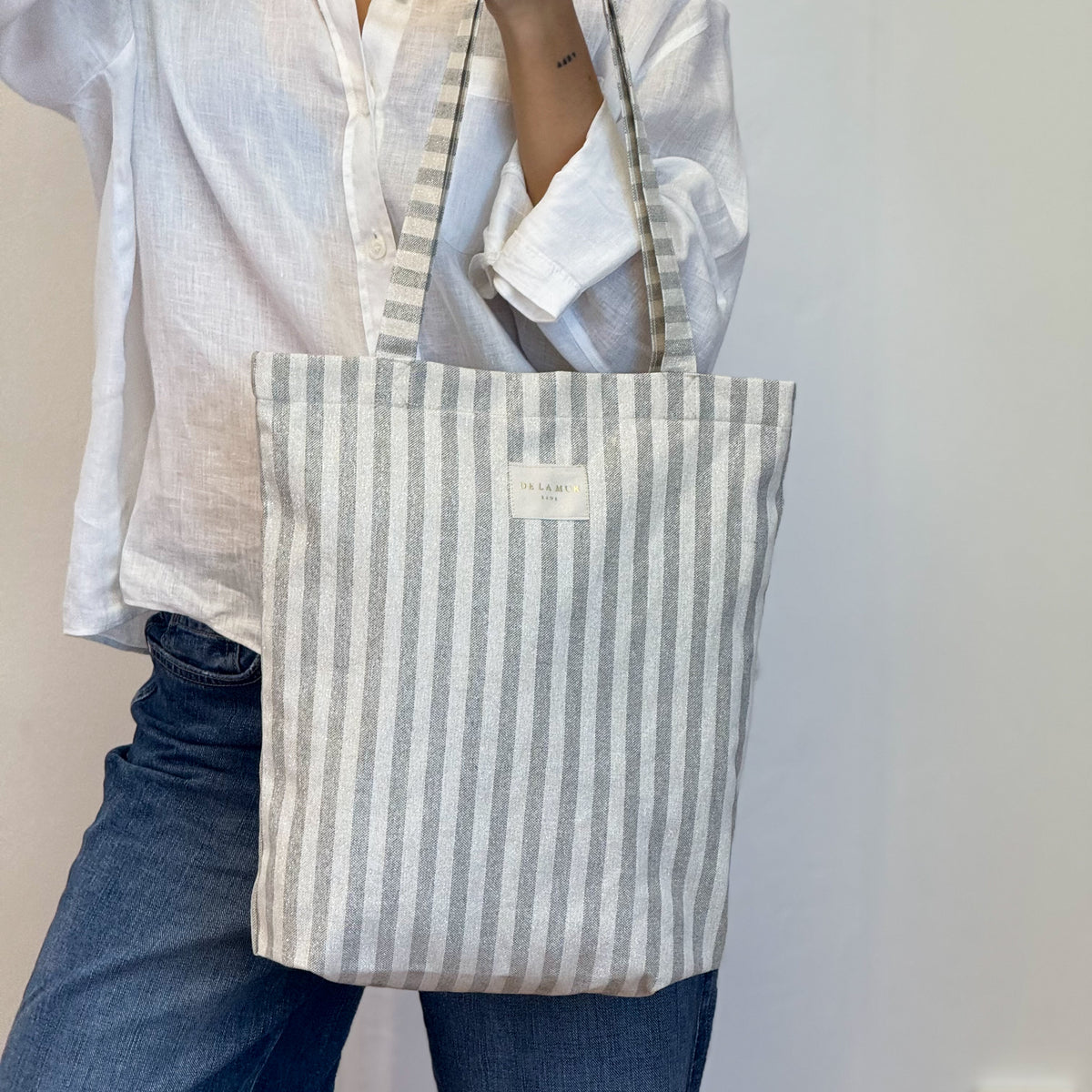 Model carrying the DE LA MUR Lugris gray and gold striped shoulder bag
