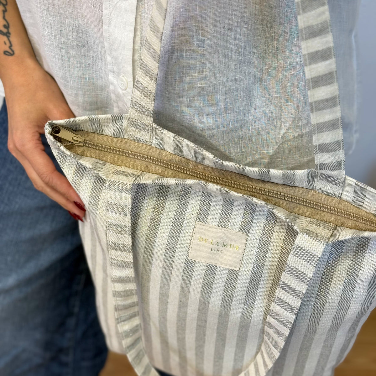 Hands opening the zip of the DE LA MUR Lugris striped bag on the shoulder