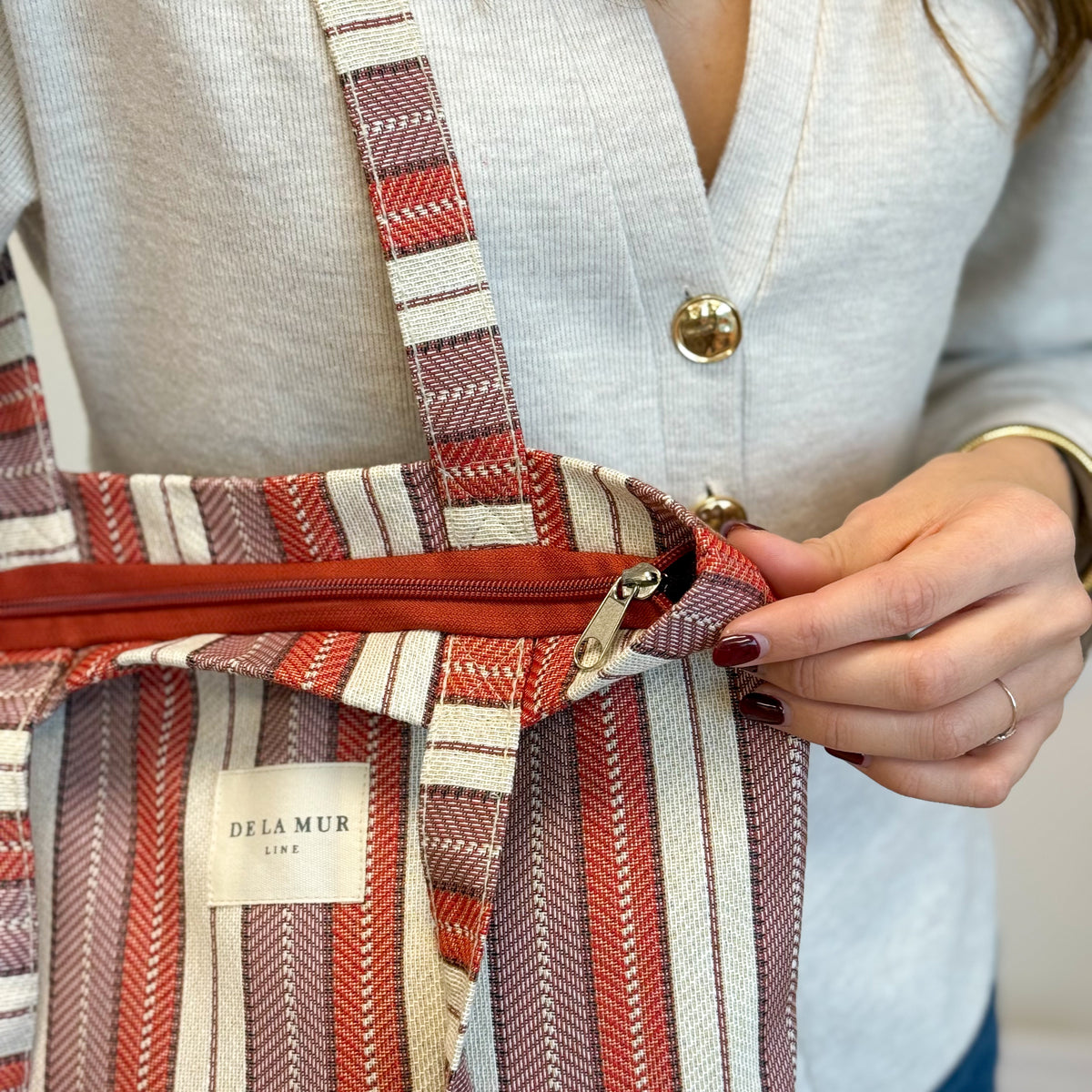 Hands opening the zip of the DE LA MUR Make striped jacquard bag
