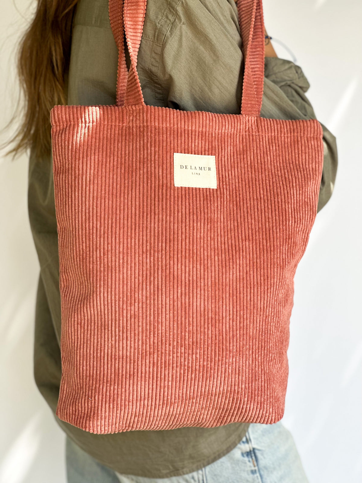 Close-up of model holding the DE LA MUR coral corduroy medium tote bag