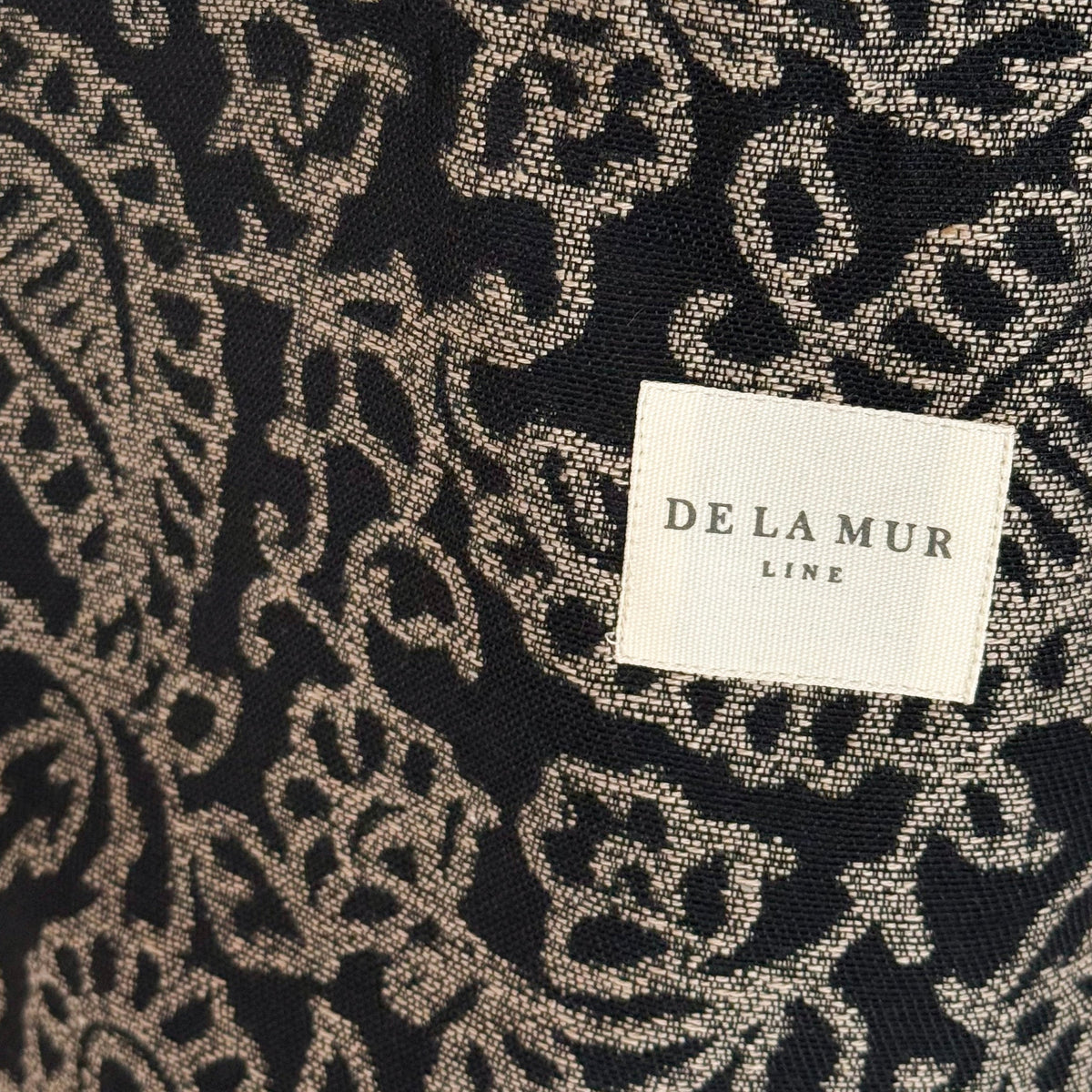 Close-up of the gray and black paisley jacquard weave and DE LA MUR label