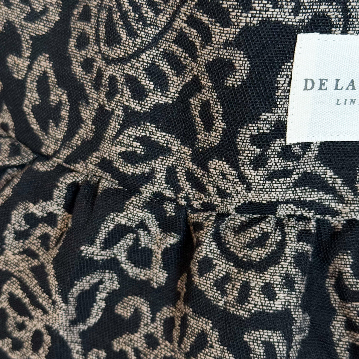 Close-up of the gray floral jacquard fabric and DE LA MUR Line label