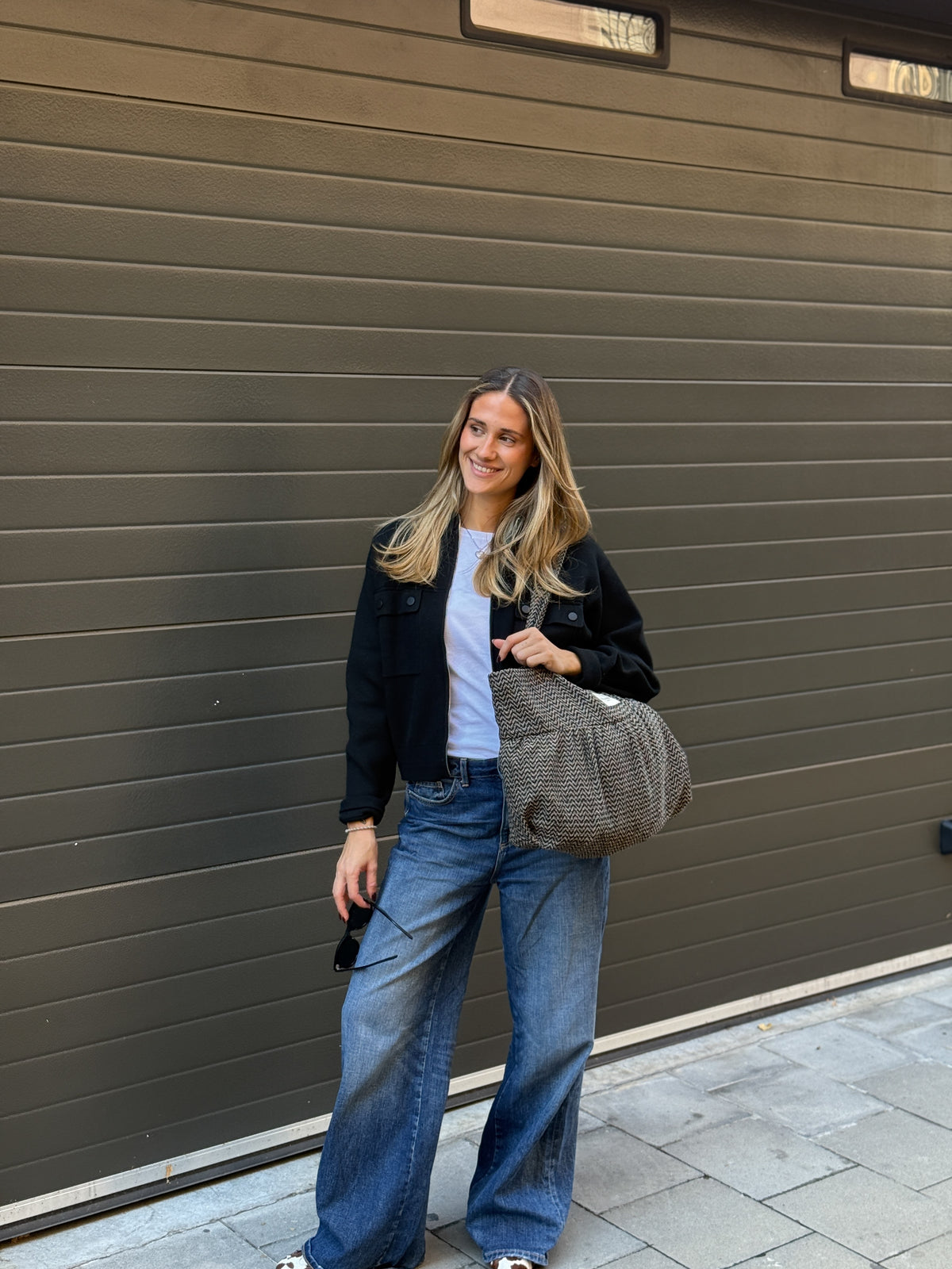 Model carrying the DE LA MUR zigzag jacquard tote bag on the shoulder outdoors