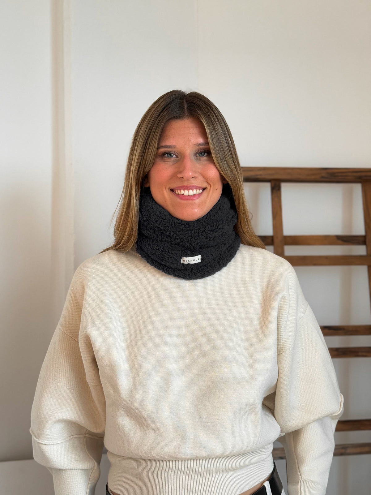 Model wearing the black DE LA MUR Kiesa sherpa neck warmer with cream sweater