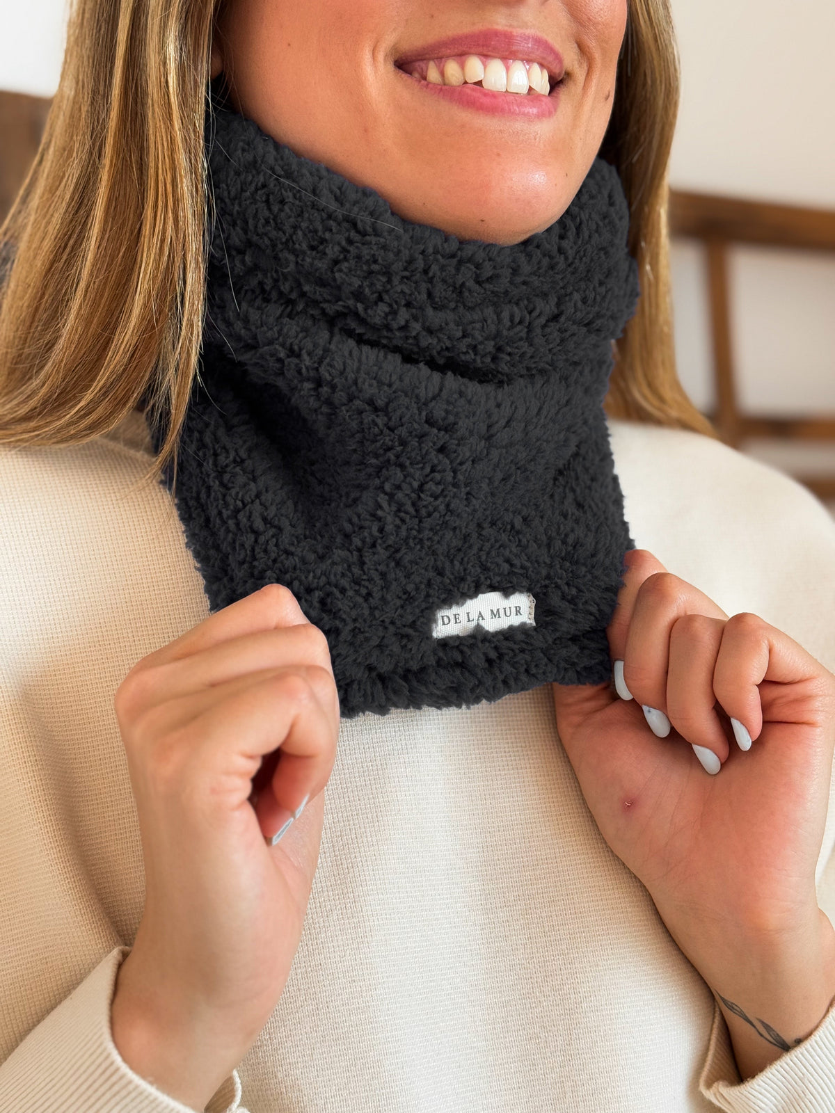 Close-up of the black fleece texture and DE LA MUR label on the Kiesa neck warmer