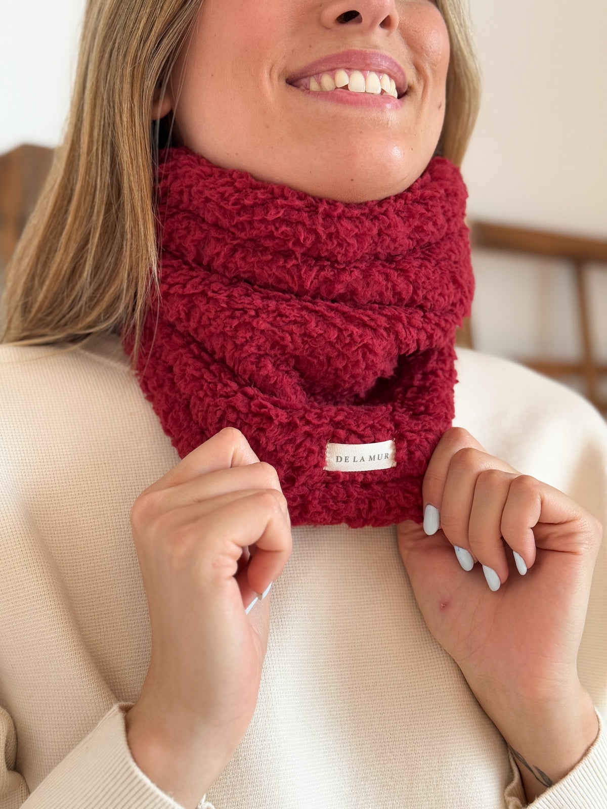 Close-up of the DE LA MUR burgundy Sherpa Neck Warmer texture and logo label
