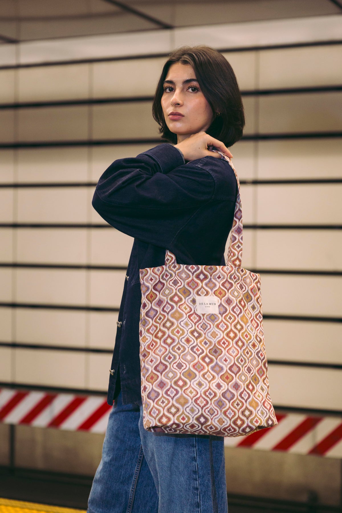 Model carrying the DE LA MUR Came medium zippered tote bag in ecru and pink over the shoulder in a styled setting