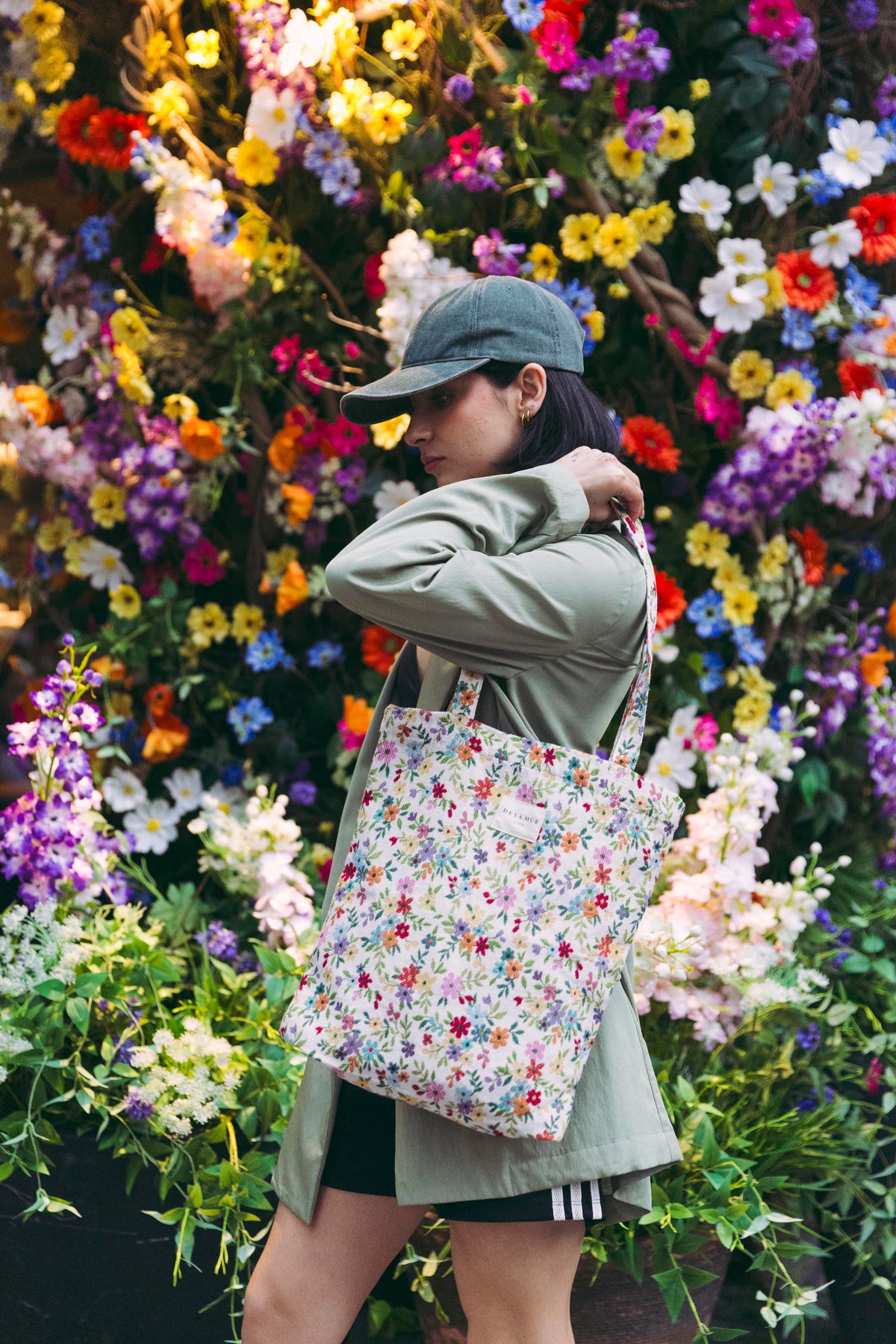 Model carrying the DE LA MUR Blum floral medium zippered tote bag over the shoulder in front of a flower wall