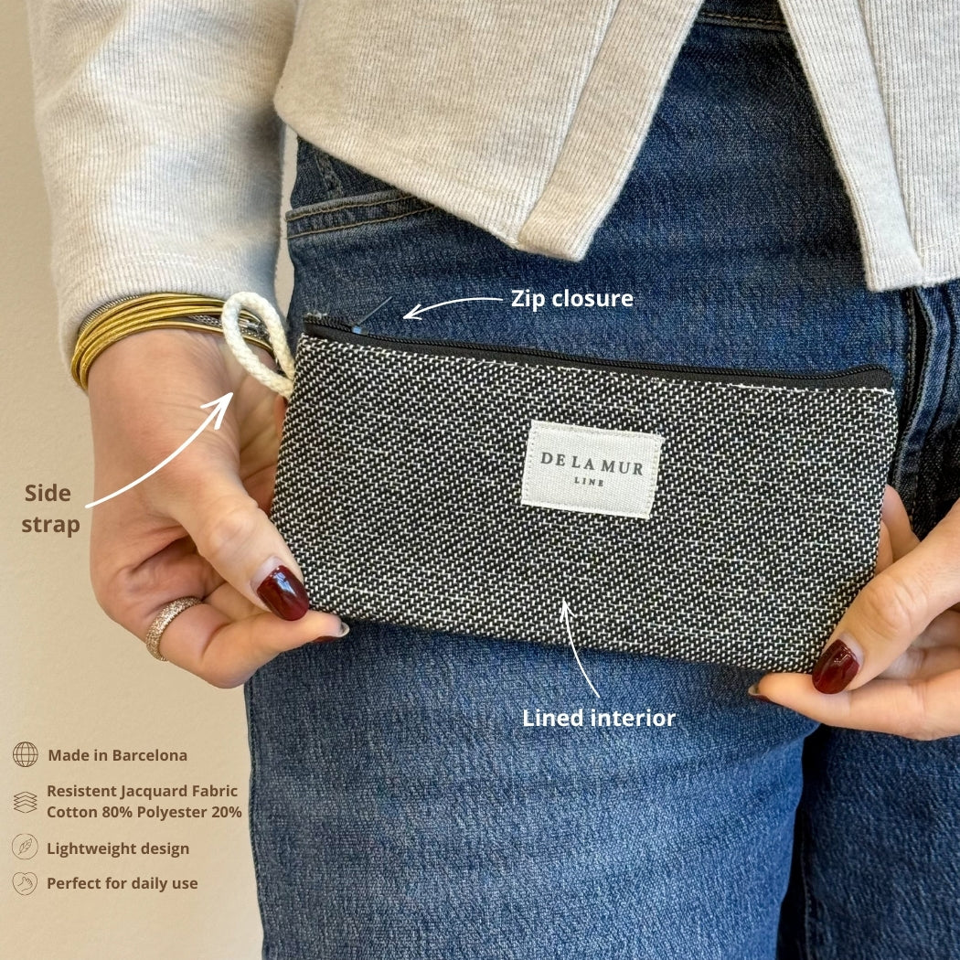 Model holding the DE LA MUR Sinay dark gray eyewear case showing zip closure and side strap