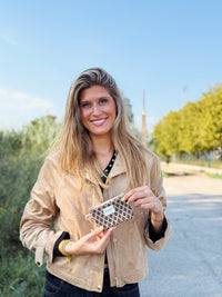 Smiling model holding the DE LA MUR beige and brown jacquard coin purse outdoors