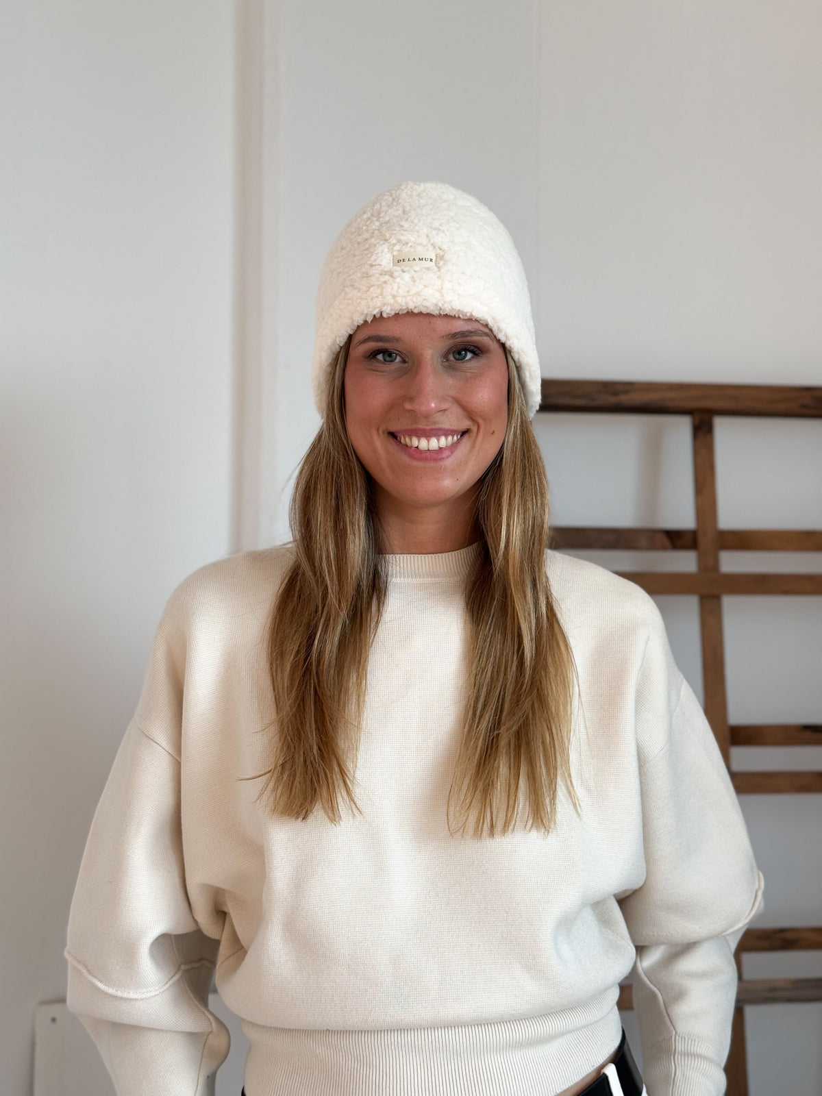 Model wearing the DE LA MUR off-white Sherpa Beanie, front view with logo label