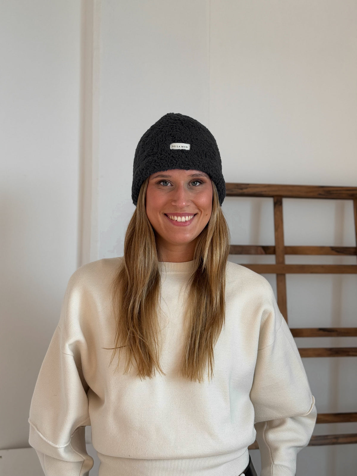 Model wearing the DE LA MUR black Sherpa Beanie, front view with logo label