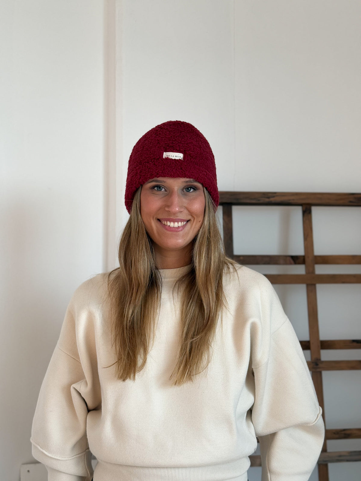 Model wearing the DE LA MUR burgundy Sherpa Beanie, front view with logo label