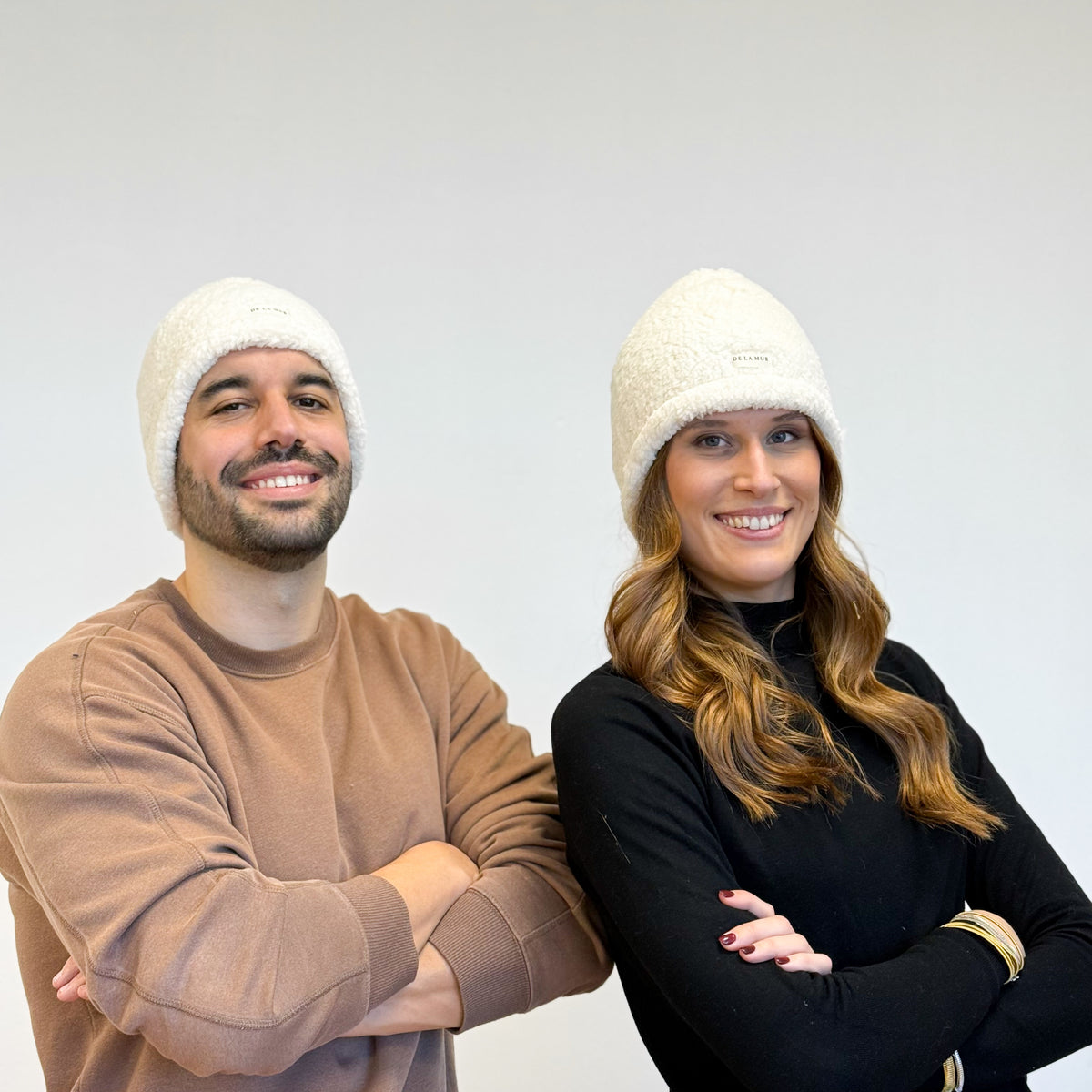 Two models wearing the DE LA MUR Sherpa Beanie in off-white, lifestyle shot