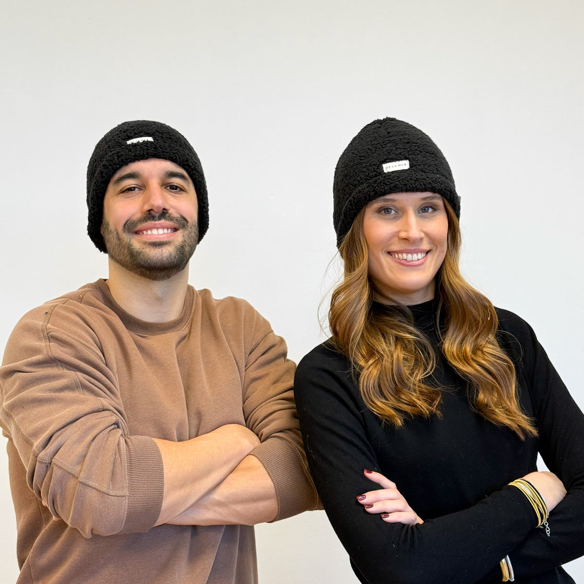 Two models wearing the DE LA MUR Sherpa Beanie in black, lifestyle shot