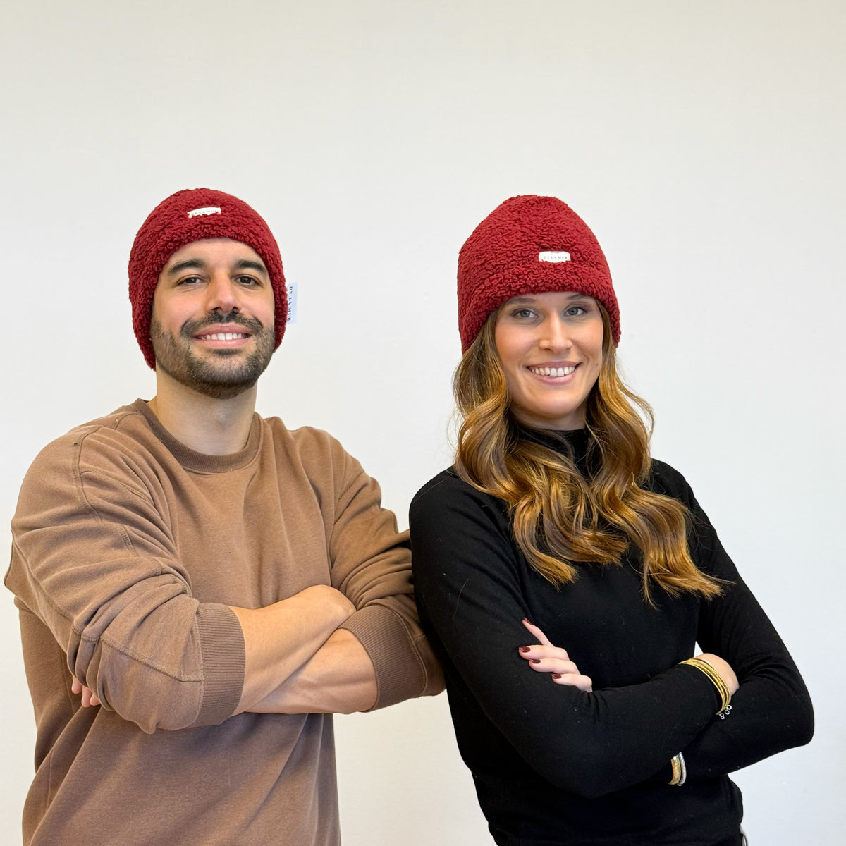 Two models wearing the DE LA MUR Sherpa Beanie in burgundy, lifestyle shot