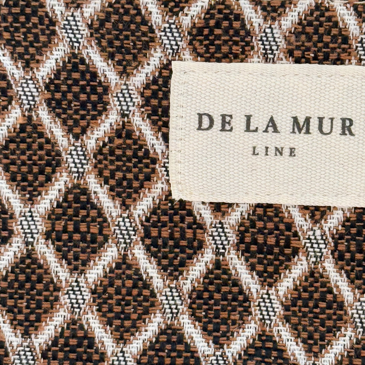 Close-up of the beige and brown geometric jacquard weave and DE LA MUR label