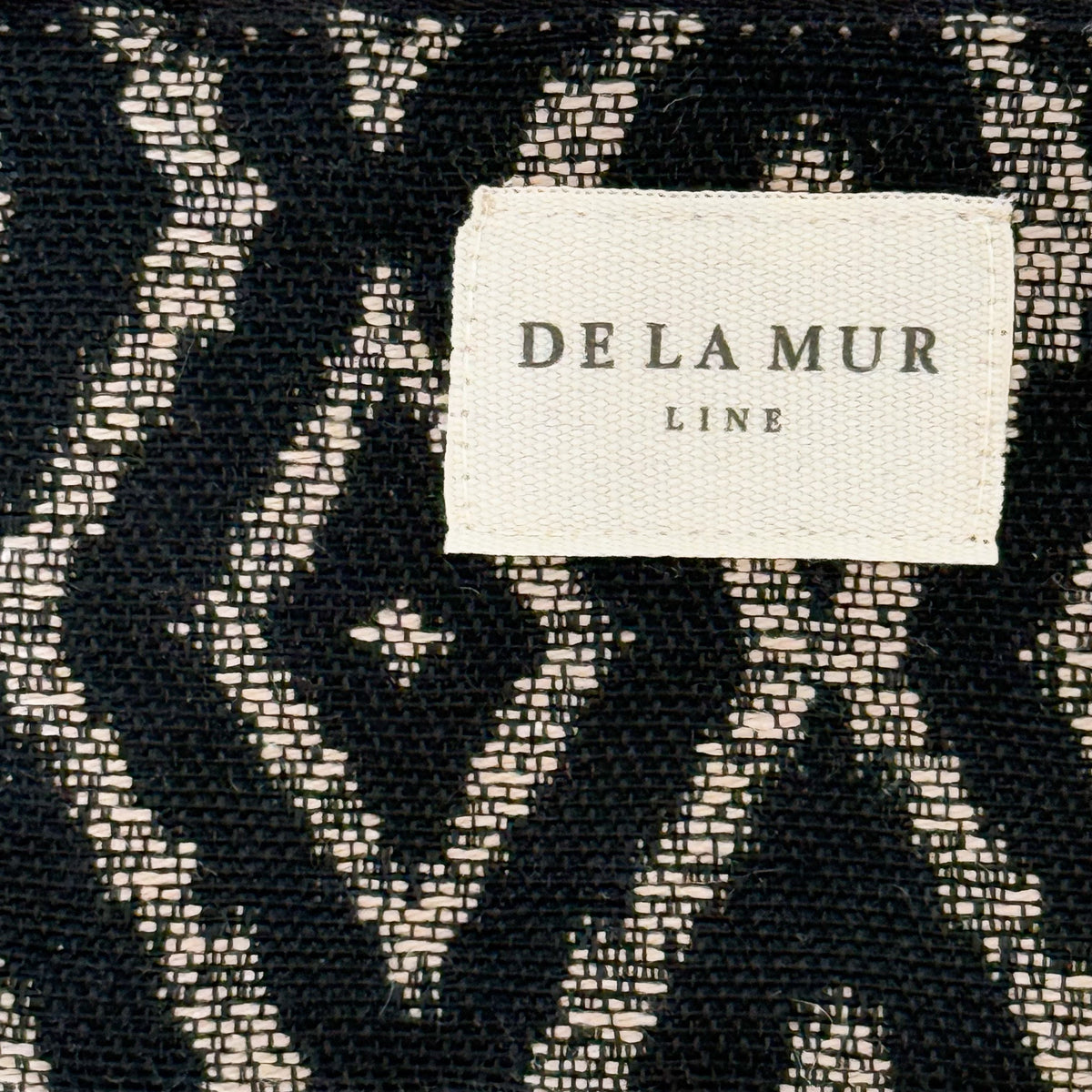 Close-up of the black and beige geometric jacquard weave and DE LA MUR label