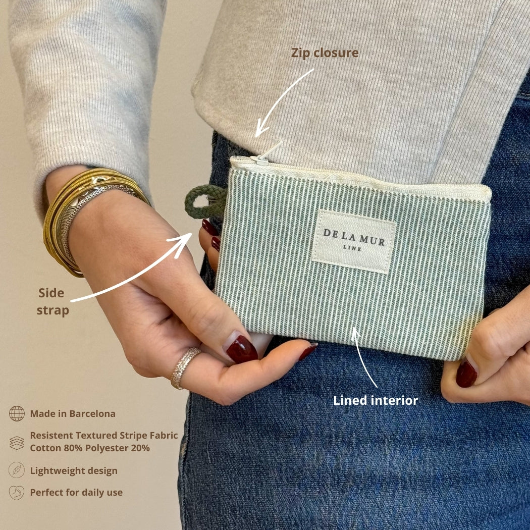 Model holding DE LA MUR Teo green striped coin purse showing side strap and zip