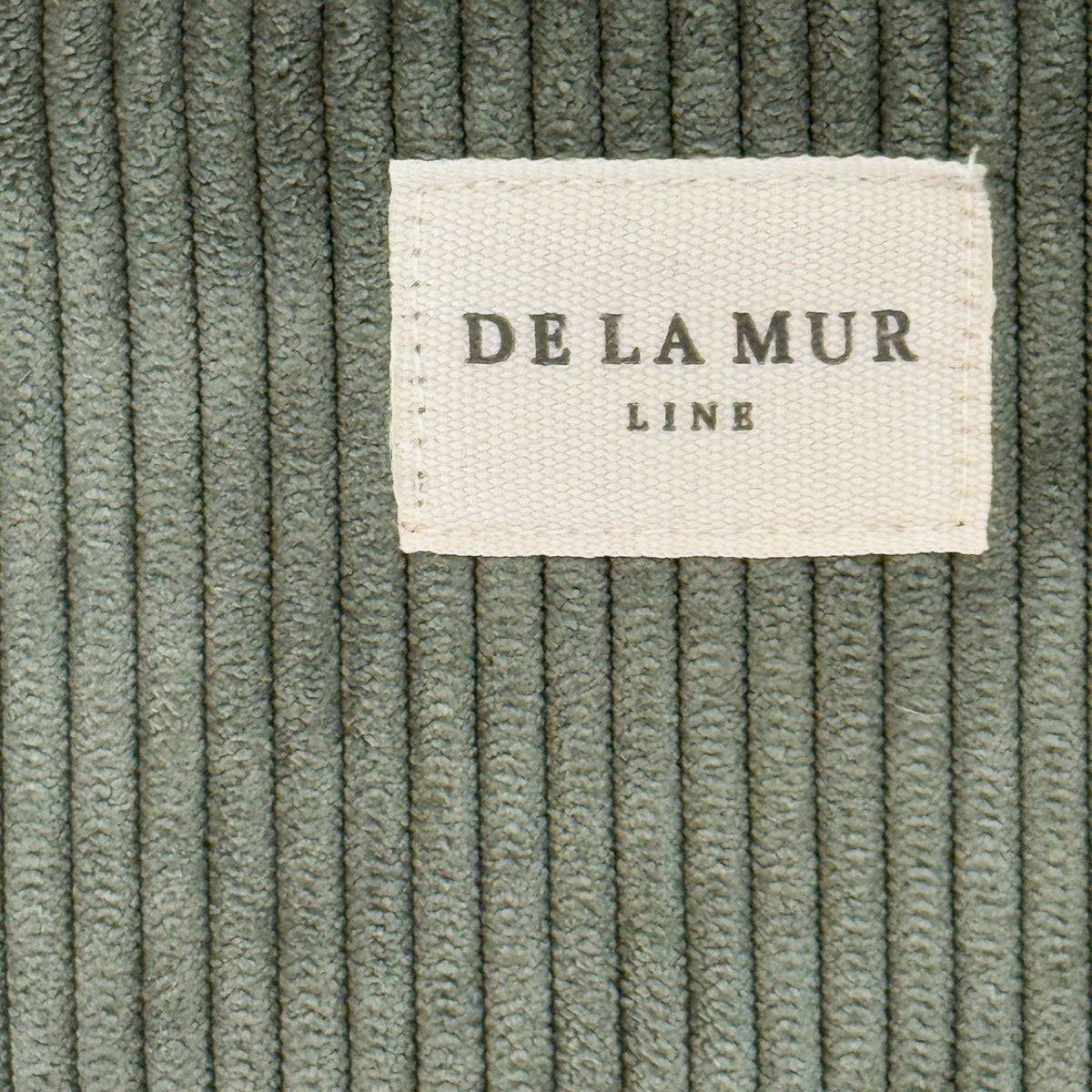 Close-up of green corduroy fabric and DE LA MUR Line label