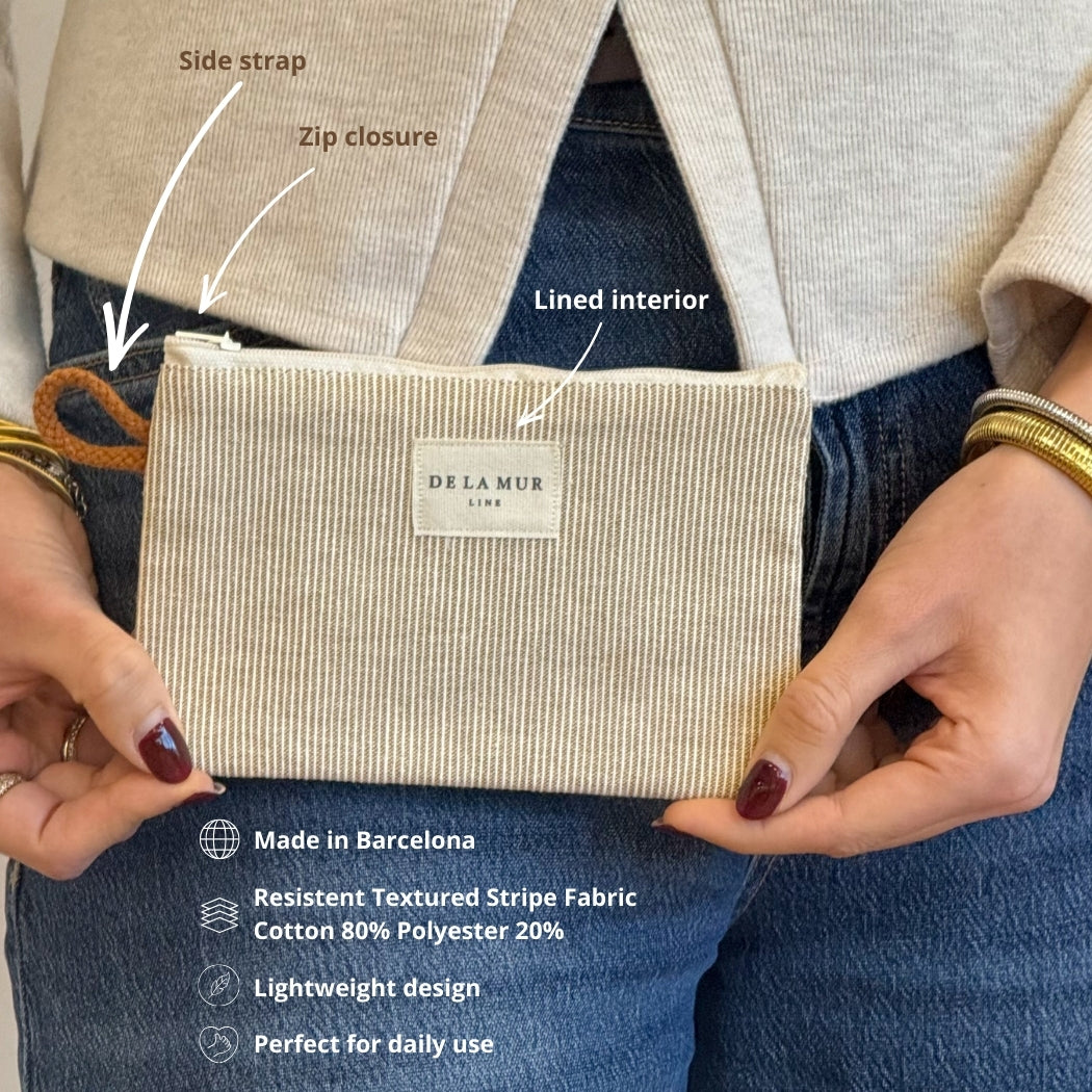 Model holding the DE LA MUR Foz striped makeup bag with side strap and material callouts