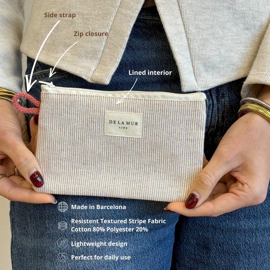 Model holding the DE LA MUR Ibi striped makeup bag with side strap and feature callouts