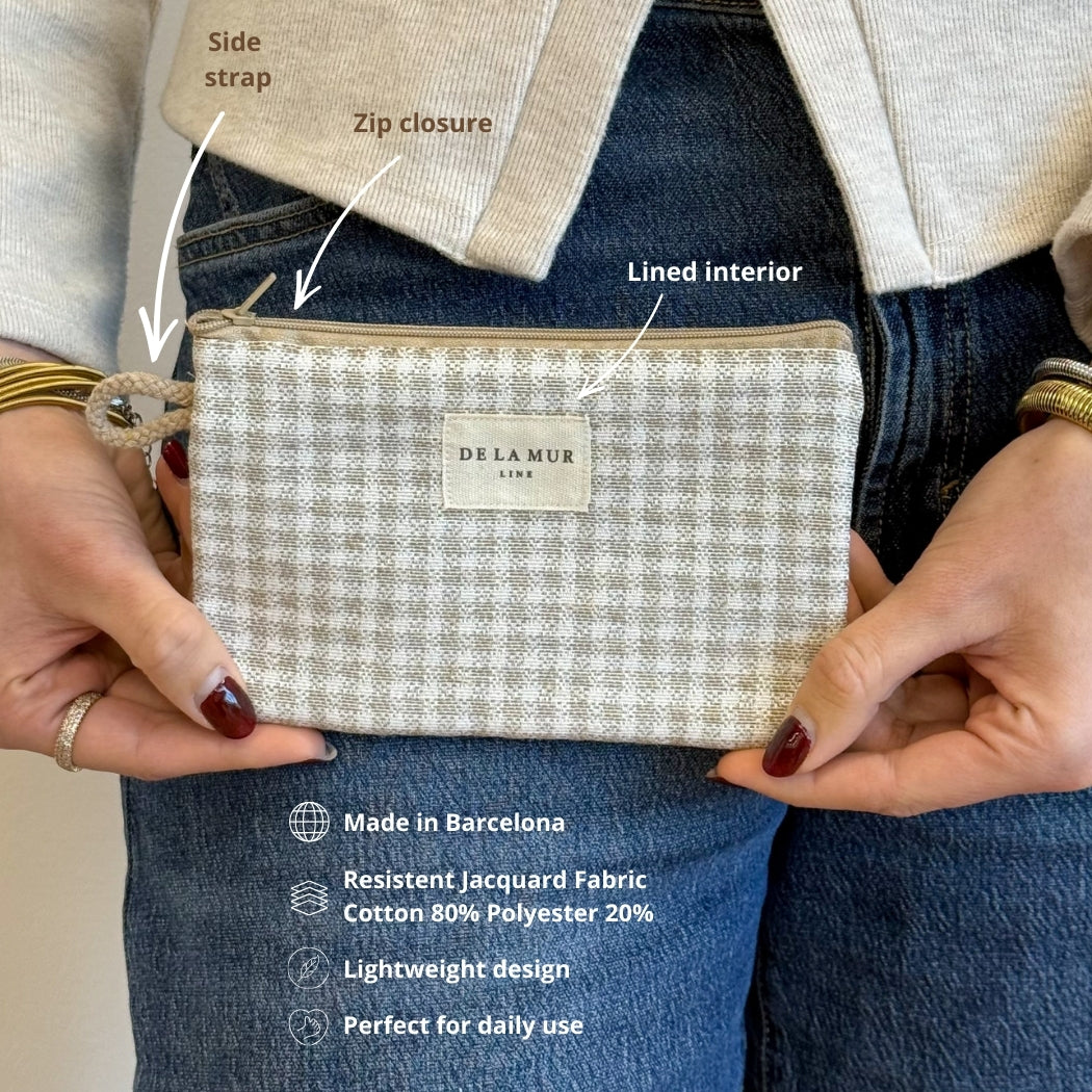 Model holding DE LA MUR Vison check pouch, side strap and zip closure labeled